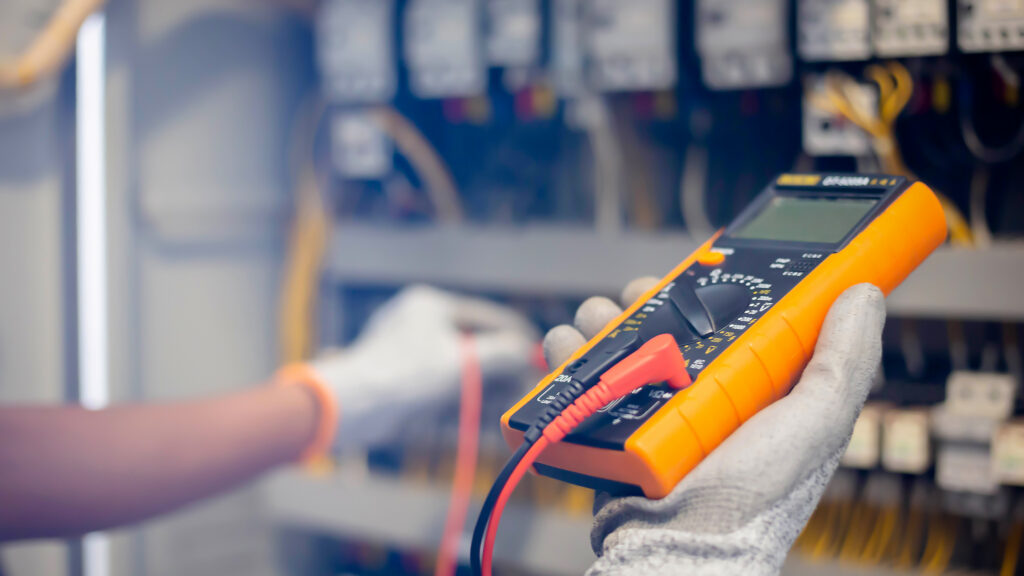 Electrician engineer uses a multimeter to test the electrical installation and power line current in an electrical system control cabinet. Multimeter Calibration.